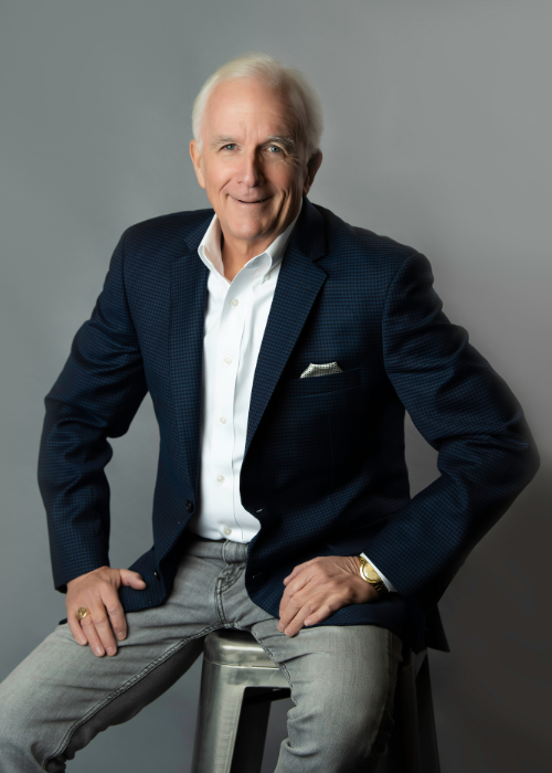 Executive man in modern company headshot gray background sitting on stool